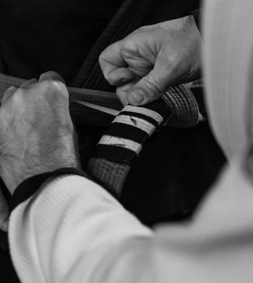 Hands tying a striped Brazilian Jiu Jitsu belt, black and white