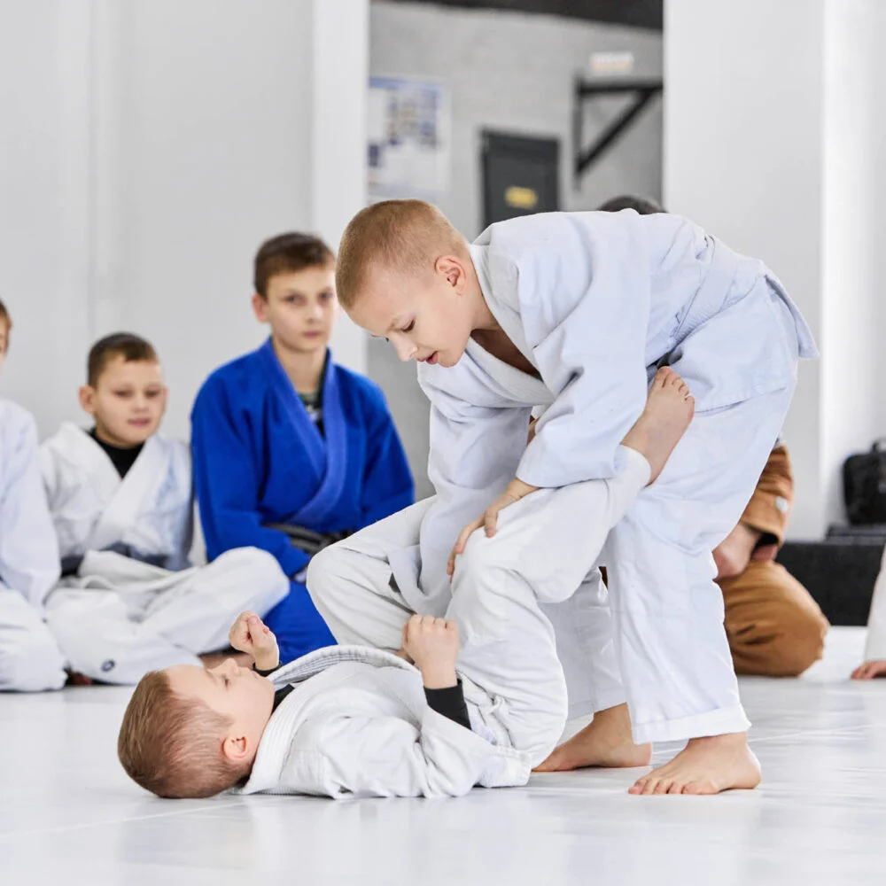 Kids in gis drilling a guard pass while classmates watch