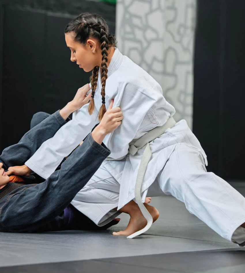 Two women training Brazilian Jiu Jitsu in gis, one working from guard